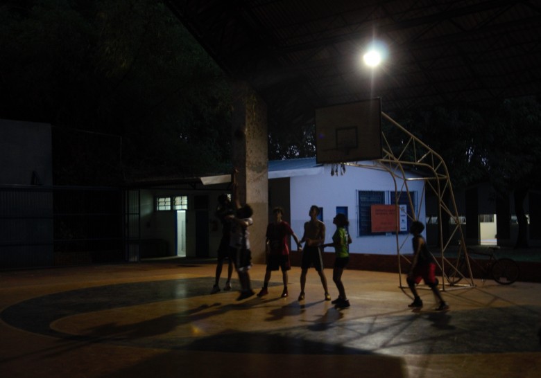 Jovens jogam basquete com iluminação precária